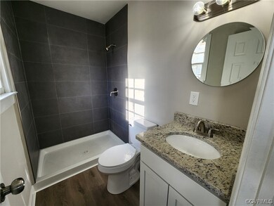 Bathroom featuring toilet, large vanity, tiled shower, and wood-type flooring