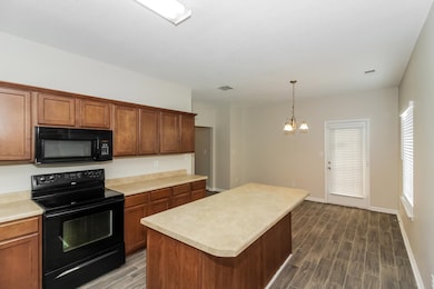 Kitchen featuring black appliances, wood finish floors, light countertops, hanging light fixtures, and a kitchen island