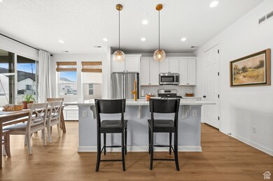 Kitchen with a center island with sink, white cabinetry, appliances with stainless steel finishes, backsplash, and pendant lighting