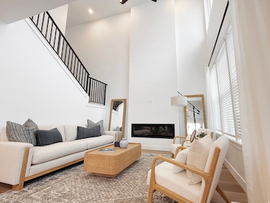 Living area with wood finished floors, a high ceiling, a ceiling fan, a glass covered fireplace, and stairs