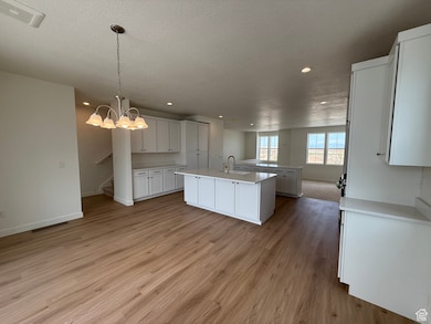 Kitchen featuring light wood-style floors, a kitchen island with sink, light countertops, recessed lighting, and white cabinets