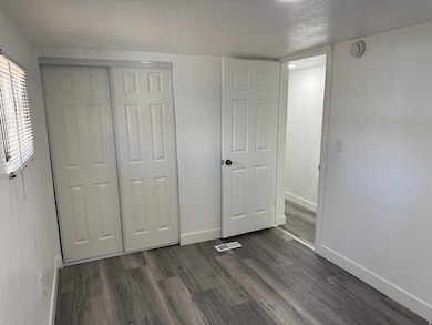 Unfurnished bedroom featuring a textured ceiling, dark wood-style floors, and a closet