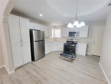 Kitchen with appliances with stainless steel finishes, white cabinetry, light wood-style floors, light countertops, and hanging light fixtures