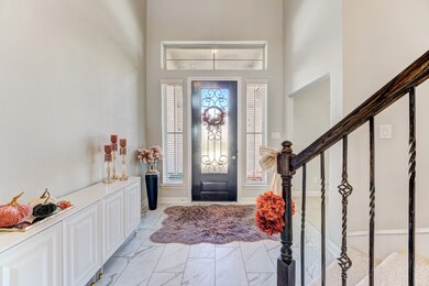 Inviting entryway with high ceilings, decorative iron door, and side windows for natural light. Features elegant staircase, marble-style flooring, and seasonal decor accents.