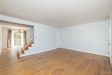 Empty room featuring a chandelier, stairway, hardw