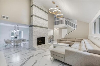 Living room featuring a stone fireplace, a towering ceiling, and a notable chandelier