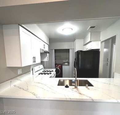 Kitchen featuring light stone counters, white range with gas cooktop, black refrigerator, white cabinetry, and washer / dryer