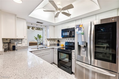 Kitchen featuring black appliances, light stone counters, a ceiling fan, white cabinets, and backsplash