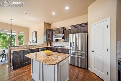 Kitchen with appliances with stainless steel finishes, a peninsula, under cabinet range hood, dark wood-type flooring, and recessed lighting