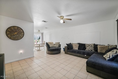 Living room with a textured ceiling, light tile patterned floors, and ceiling fan