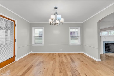 Unfurnished dining area featuring arched walkways, light wood finished floors, a premium fireplace, crown molding, and plenty of natural light