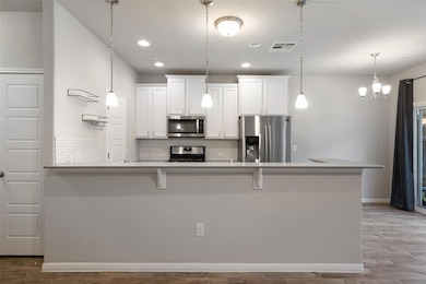 Kitchen featuring white cabinets, stainless steel appliances, backsplash, a breakfast bar, and visible vents