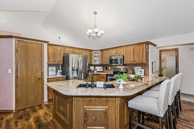 Kitchen with brown cabinetry, stainless steel appliances, decorative backsplash, a chandelier, and lofted ceiling