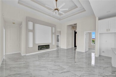 Unfurnished living room featuring light marble finish flooring, ceiling fan, baseboards, a tray ceiling, and a towering ceiling