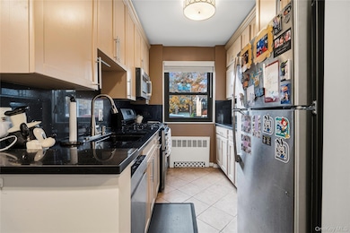 Kitchen with appliances with stainless steel finishes, light tile patterned floors, radiator, and decorative backsplash