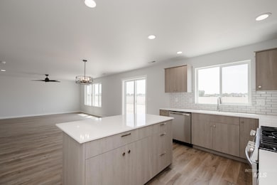 Kitchen with decorative backsplash, appliances with stainless steel finishes, light brown cabinetry, recessed lighting, and decorative light fixtures