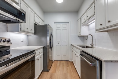 Kitchen featuring stainless steel appliances, light wood finished floors, light stone counters, and white cabinetry