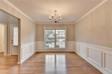 Empty room featuring a chandelier, wood finished floors, a wainscoted wall, ornamental molding, and a decorative wall