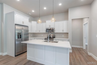 Kitchen with stainless steel appliances, white cabinetry, light wood-style flooring, a kitchen island with sink, and decorative light fixtures