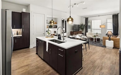 Kitchen with light wood-type flooring, stainless steel appliances, sink, pendant lighting, and a center island with sink