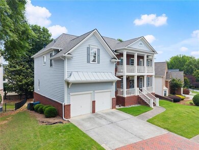 Greek revival inspired property featuring a balcony, brick siding, concrete driveway, a standing seam roof, and a garage