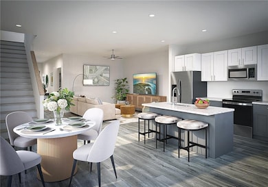 Kitchen with a breakfast bar area, a center island with sink, a ceiling fan, appliances with stainless steel finishes, and wood finished floors