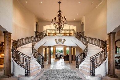 A grand marble double staircase makes an exceptional first impression in the inviting foyer featuring a custom chandelier, antiqued wood columns and limestone flooring.