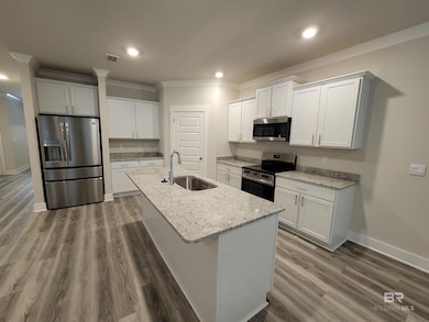 Kitchen featuring white cabinetry, stainless steel appliances, light stone countertops, ornamental molding, and a center island with sink