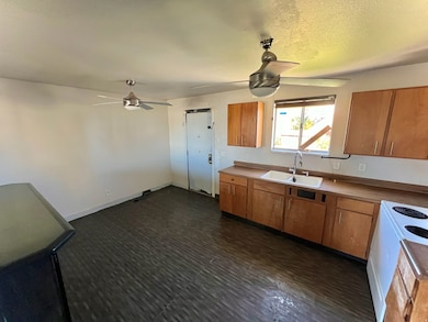 Kitchen with brown cabinets, a ceiling fan, white electric range, a textured ceiling, and light countertops