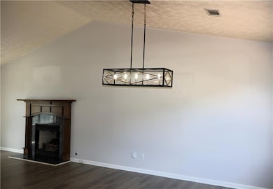 Unfurnished living room featuring dark wood-type flooring, vaulted ceiling, a fireplace with raised hearth, a textured ceiling, and a chandelier