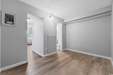 Empty room with wood finished floors, a textured ceiling, and baseboards
