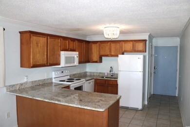 Kitchen featuring white appliances, a sink, brown cabinetry, a peninsula, and a textured ceiling
