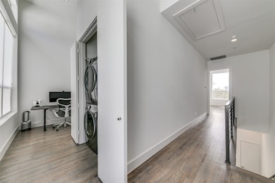 Hall featuring stacked washing machine and dryer, an office area, attic access, light wood finished floors, and an upstairs landing