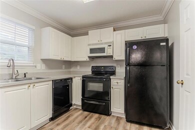 Kitchen featuring black appliances, a sink, white cabinetry, ornamental molding, and light countertops