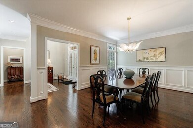 Dining room with crown molding, a chandelier, a wainscoted wall, dark wood-style floors, and a decorative wall