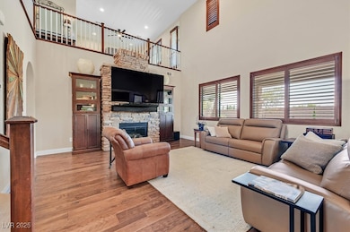 Living room featuring light wood-type flooring, a high ceiling, a stone fireplace, and recessed lighting