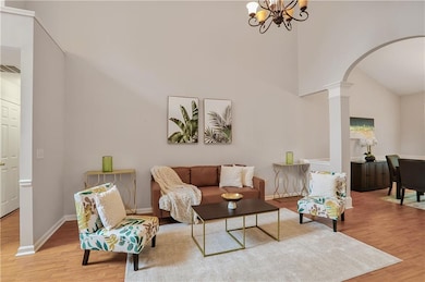 Living room featuring arched walkways, wood finished floors, ornate columns, high vaulted ceiling, and a chandelier