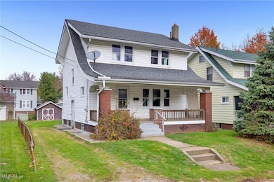 View of front facade featuring a porch, a chimney, a shingled roof, and a storage shed