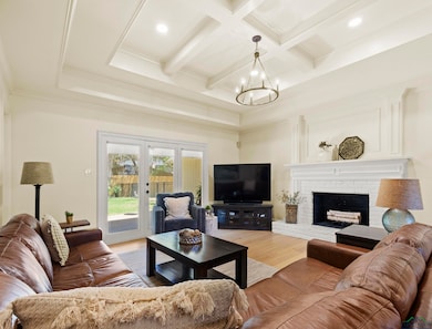 Living area with light wood-style floors, crown molding, a brick fireplace, beam ceiling, and an inviting chandelier