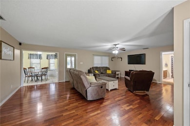 Living area with a textured ceiling, dark wood-type flooring, and ceiling fan