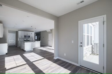 Kitchen with white cabinetry, an island with sink, pendant lighting, dark wood-style floors, and appliances with stainless steel finishes