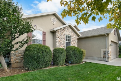 View of side of home featuring stone siding, an attached garage, stucco siding, and a yard