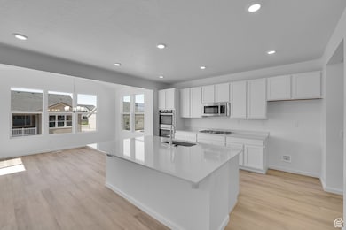Kitchen featuring white cabinets, a chandelier, recessed lighting, a center island with sink, and light wood-style flooring