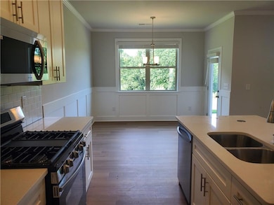 Kitchen with appliances with stainless steel finishes, light stone counters, dark wood-style flooring, crown molding, and pendant lighting