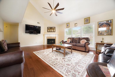 Living room featuring a ceiling fan, high vaulted ceiling, dark wood-type flooring, and a fireplace