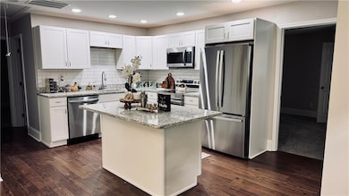 Kitchen featuring appliances with stainless steel finishes, dark wood-style flooring, light stone counters, tasteful backsplash, and recessed lighting