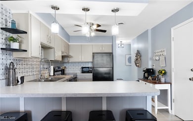 Kitchen with a peninsula, black appliances, light countertops, tasteful backsplash, and open shelves