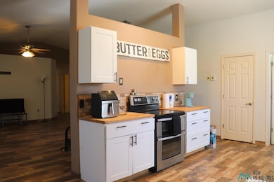 Kitchen with double oven range, white cabinets, dark wood-style floors, tasteful backsplash, and a ceiling fan