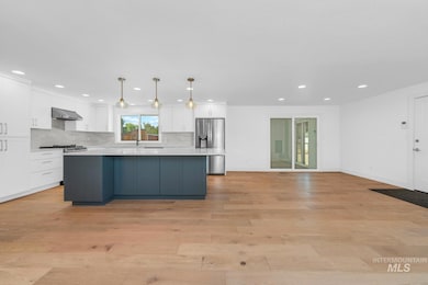 Kitchen with appliances with stainless steel finishes, a center island, white cabinets, wall chimney exhaust hood, and recessed lighting