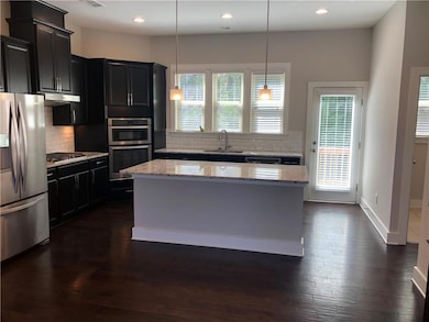 Kitchen with stainless steel appliances, decorative backsplash, a kitchen island, dark wood-type flooring, and under cabinet range hood